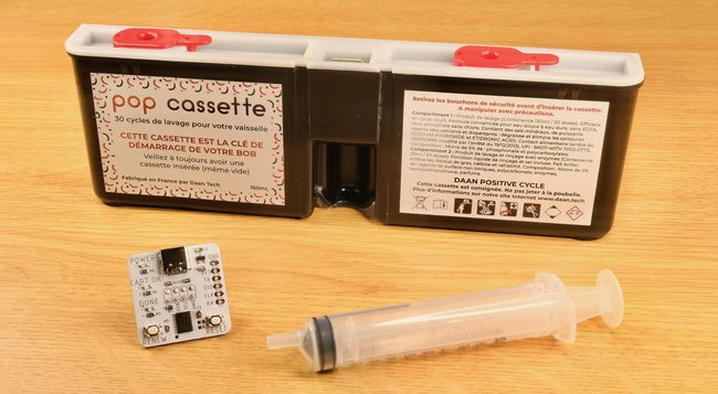 The product-shot for a Bob Cassette Rewinder, featuring a cassette, a small hardware dongle, and a refiller syringe.